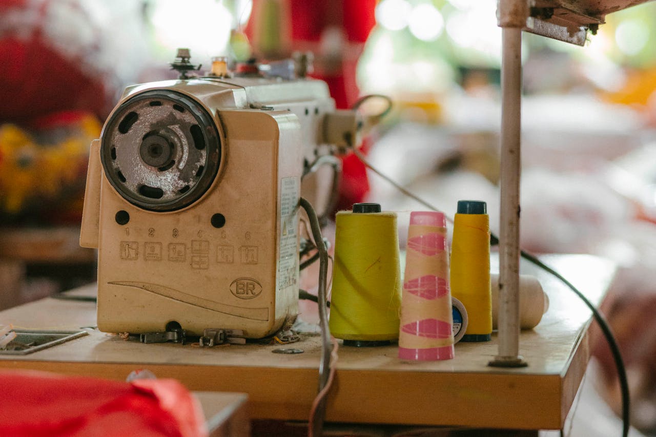Close-up of a vintage sewing machine and colorful spools of thread on a workshop table.